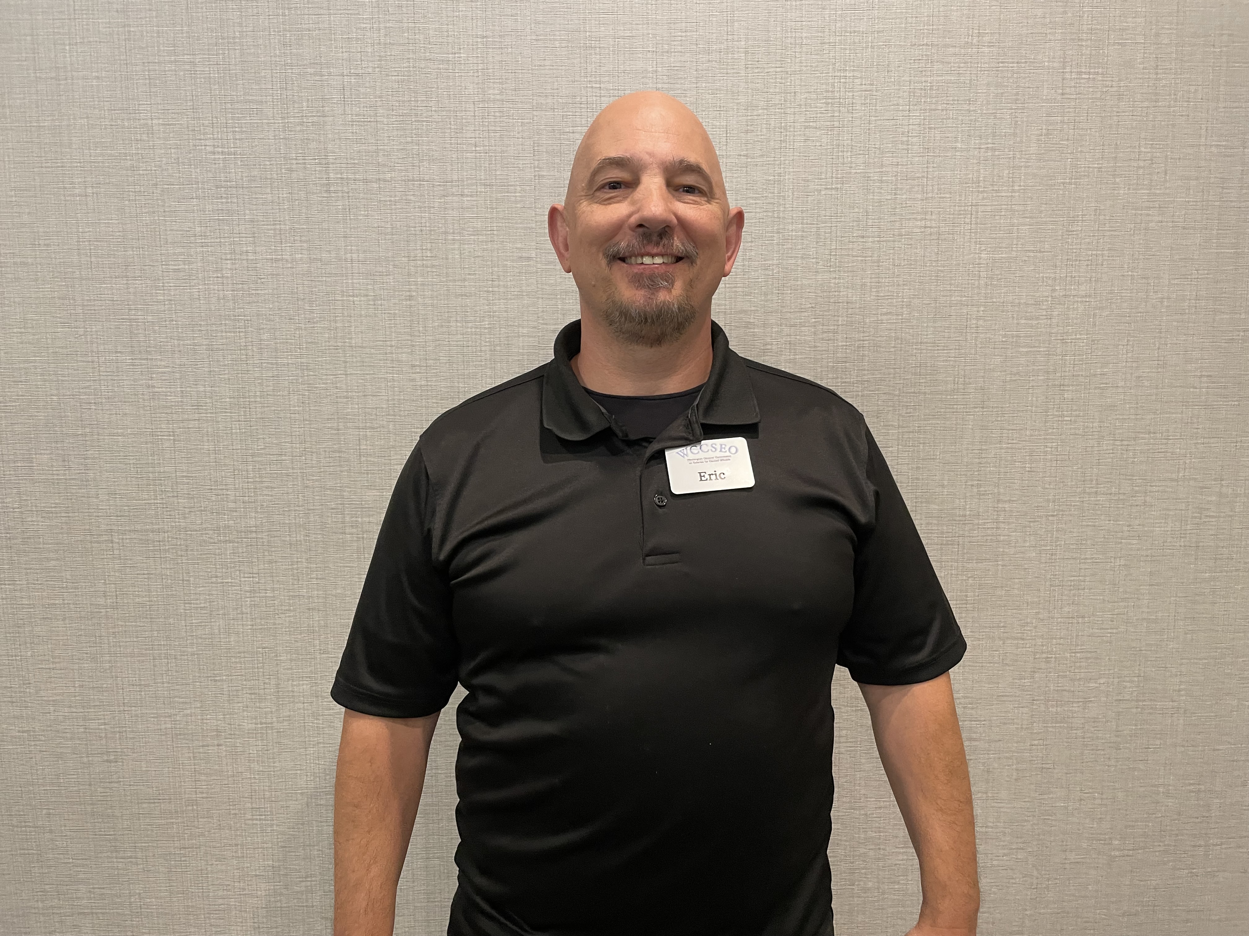 Kirby, headshot of middle-aged male with a shaved head and goatee wearing a black polo shirt