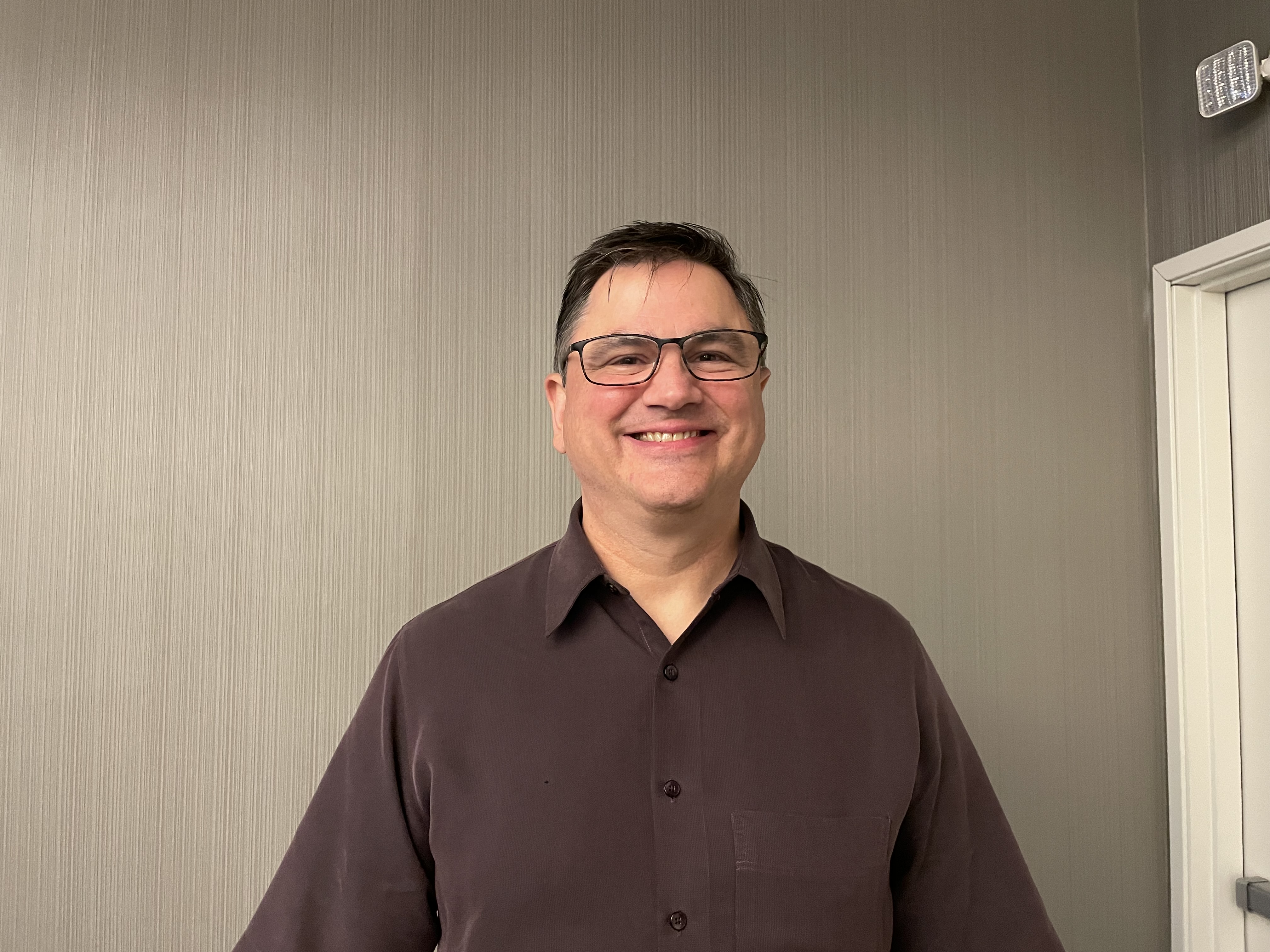 Erik, man smiling, wearing glasses and a brown collar shirt