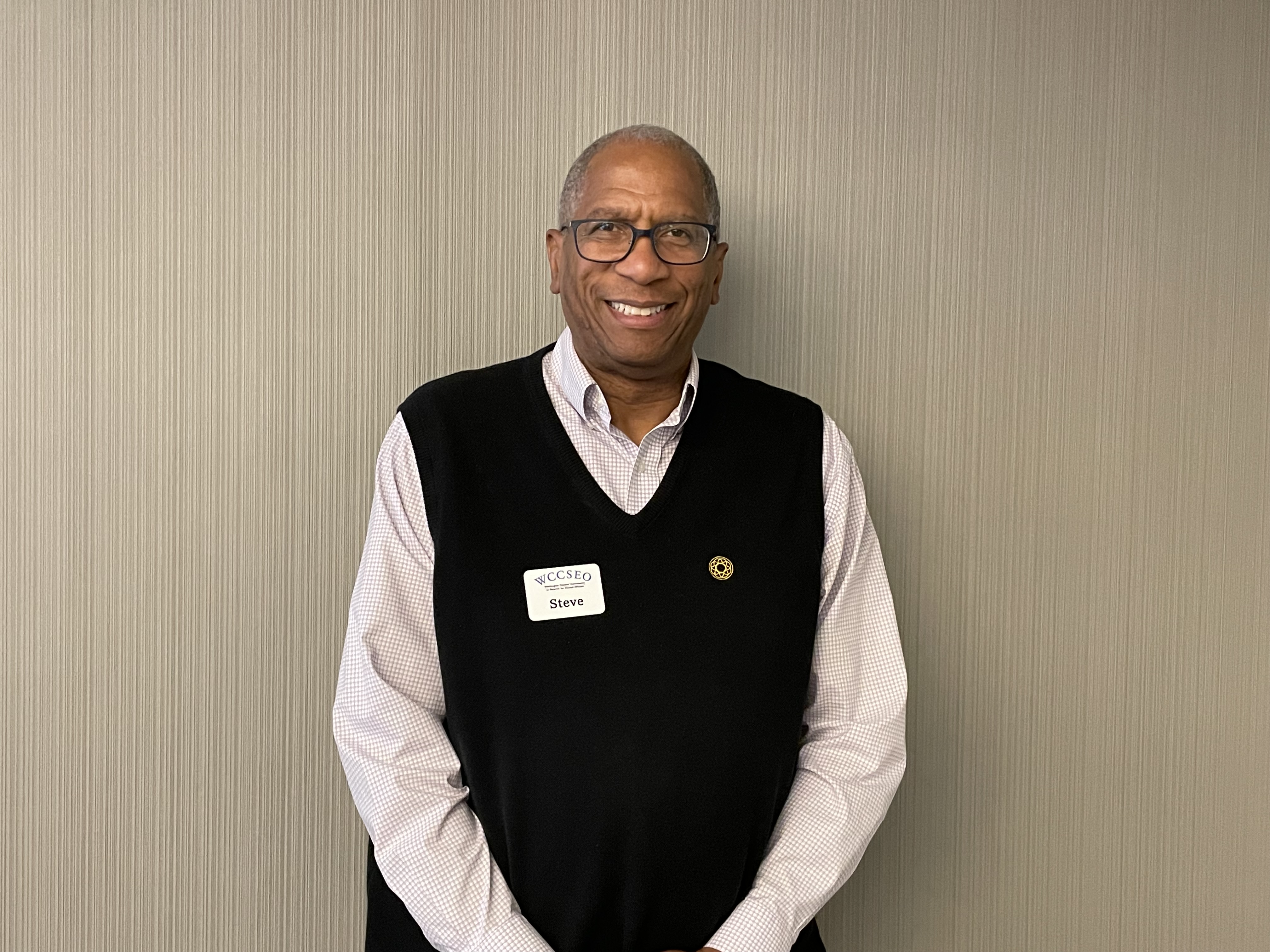 Steve, Man smiling wearing glasses, and a white collar shirt with a black vest